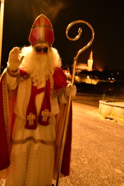 Saint-Nicolas salue de la main, la nuit, devant l'église illuminée