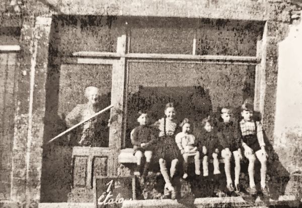 Michel et Francis Minguet, Monique, Michel et Jean-François Van Bever sont assis devant la vitrine de Marie Van Bever. Marie tient une épicerie. Elle est en…